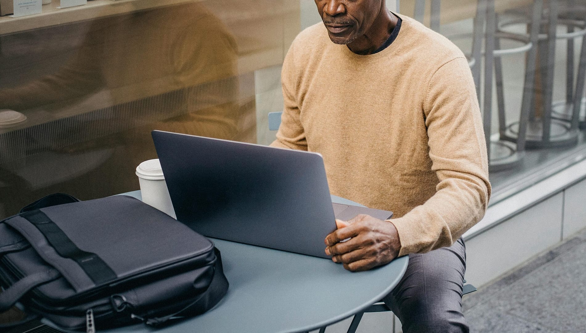 Middle-aged man using a laptop at an outdoor café, focused on work with a coffee.